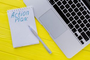Modelo de plano de ação simples em caderno ao lado de notebook para acompanhamento de prazos operacionais.