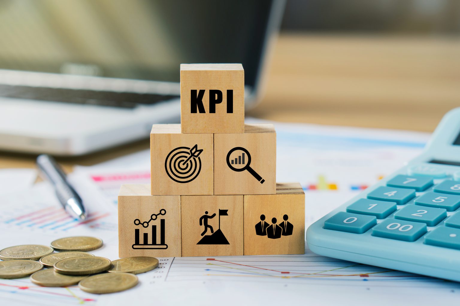 KPIs representados por blocos de madeira sobre relatórios financeiros, com calculadora e moedas, simbolizando gestão de indicadores e desempenho empresarial.