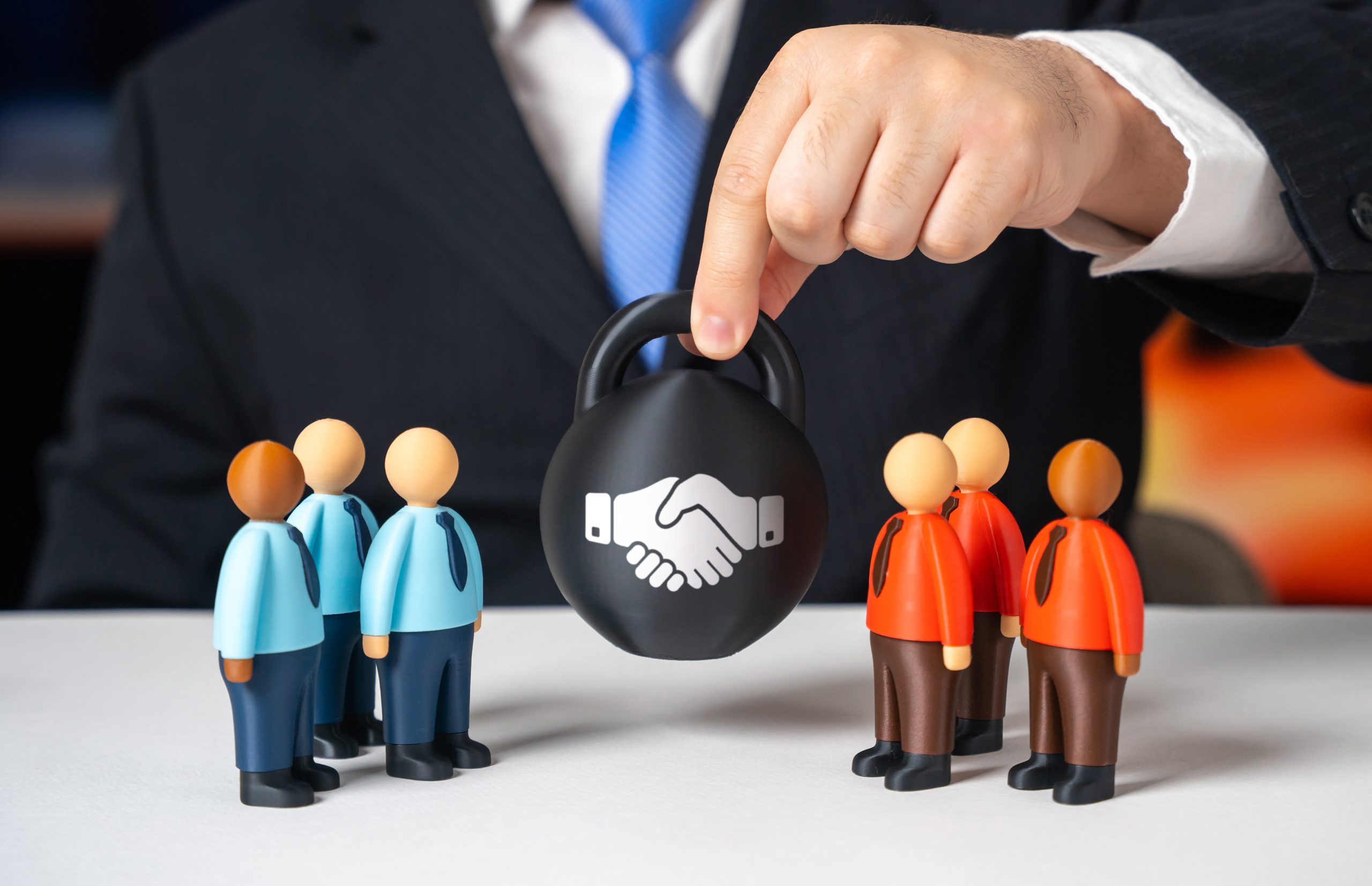 Profissional posiciona símbolo de aperto de mãos protegido entre dois grupos, representando gestão de riscos, compliance e proteção de relações comerciais.