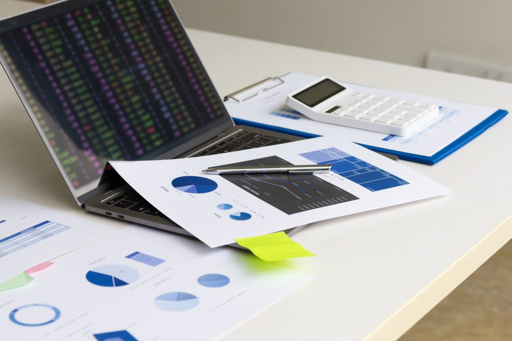 Relatórios com gráficos financeiros, notebook e calculadora sobre mesa de trabalho, representando análise de indicadores, gestão de desempenho e tomada de decisão baseada em dados.
